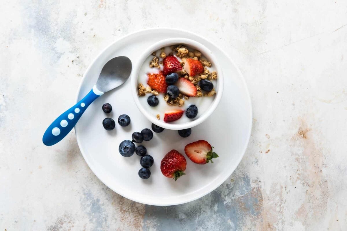 A toddler lunch of a yogurt parfait containing yogurt, berries and granola.