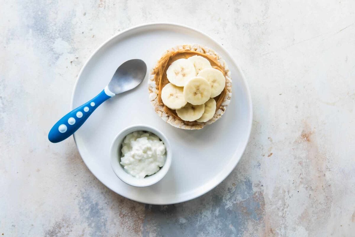 A toddler lunch of peanut butter and banana rice cake with a side of cottage cheese.