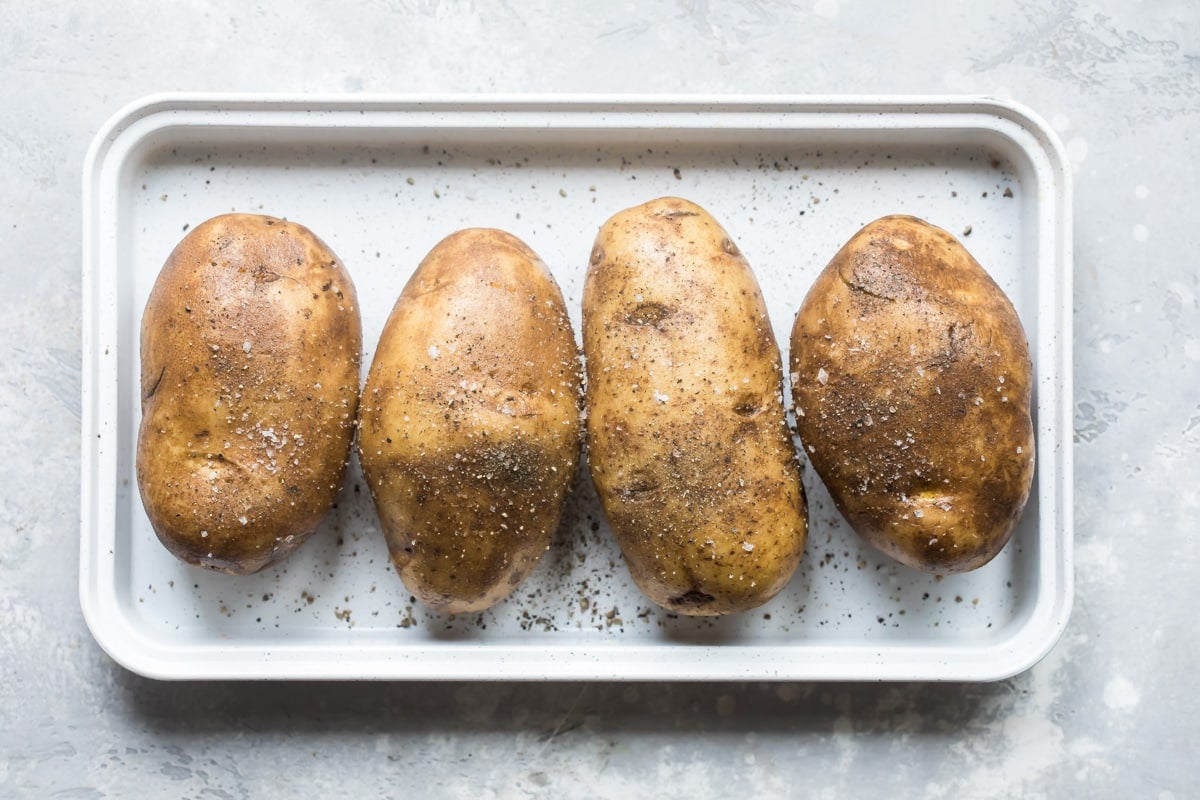 Four potatoes on a baking sheet before being baked.