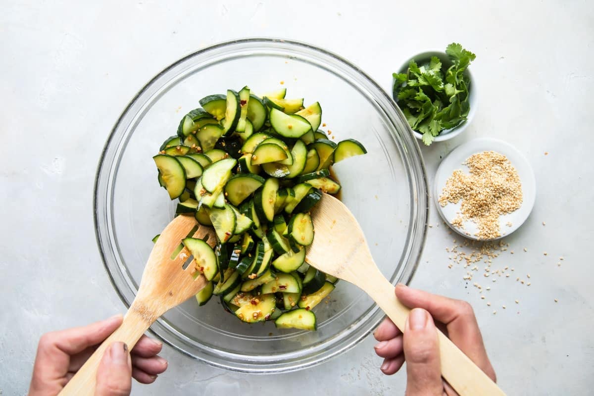 Cucumber salad being stirred in a glass bowl.