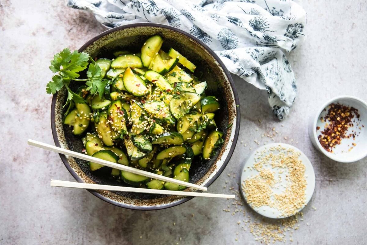 A black bowl of Asian cucumber salad with chopsticks resting on the side of the bowl.