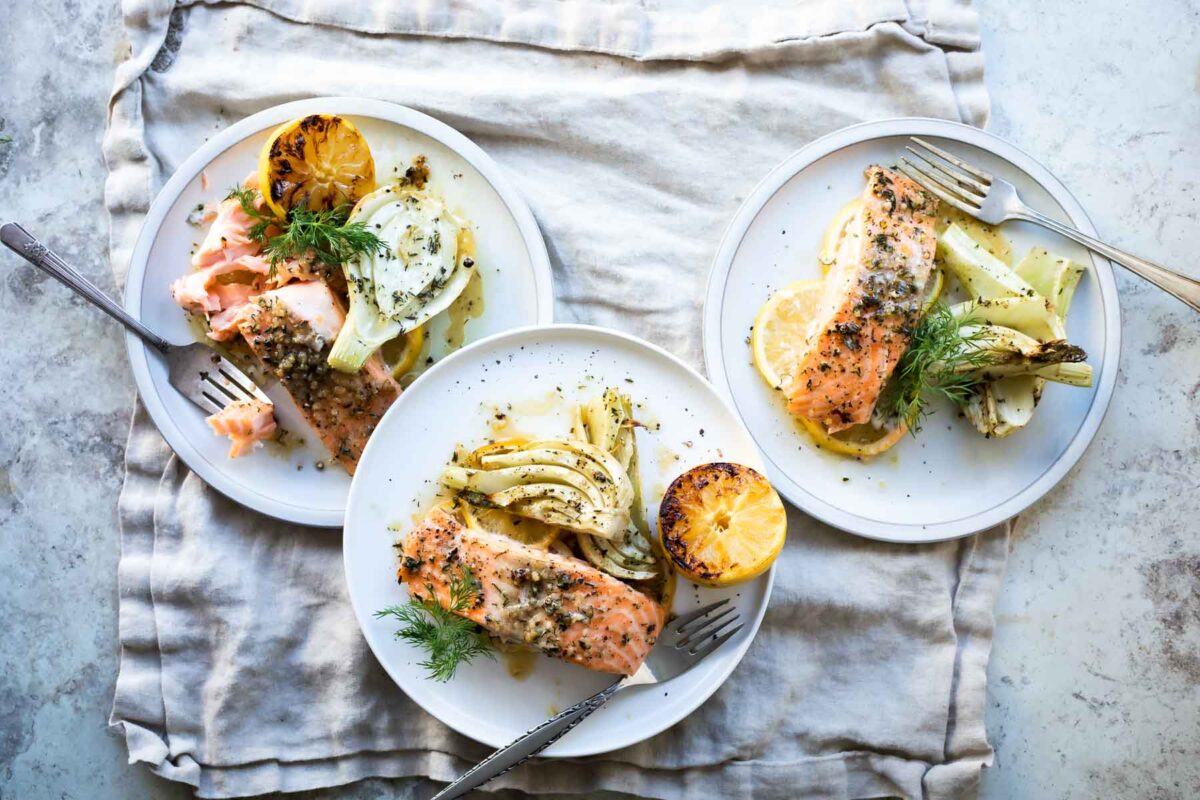 Salmon filets on three plates with roasted fennel.