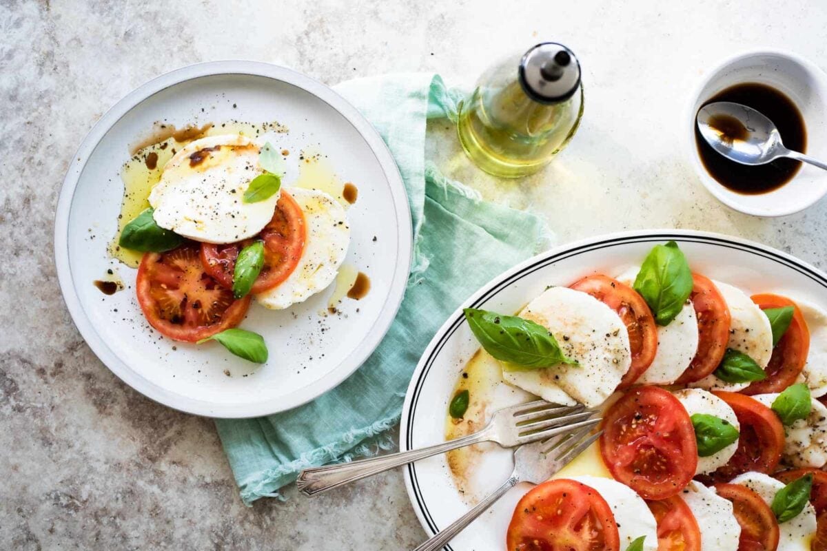 A small plate of caprese salad next to a large platter of caprese salad.