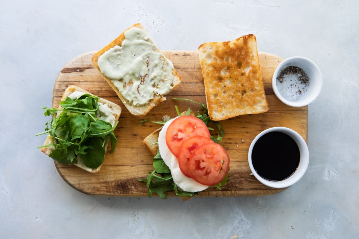 Caprese sandwiches being assembled on a wooden cutting board.