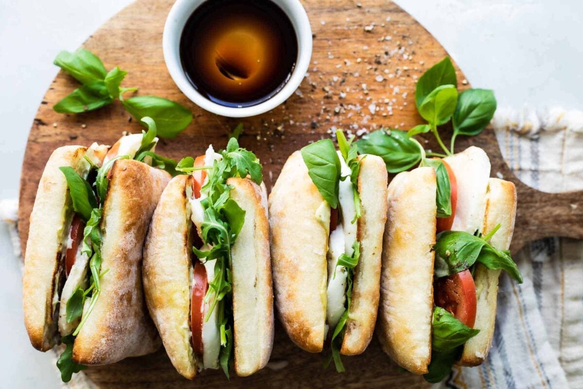 Four caprese sandwiches laying on their sides on a wooden cutting board.