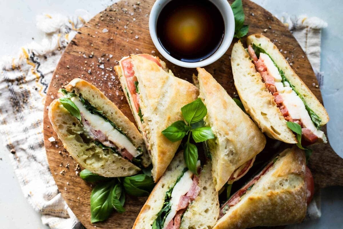 Halved caprese sandwiches on a wooden cutting board.