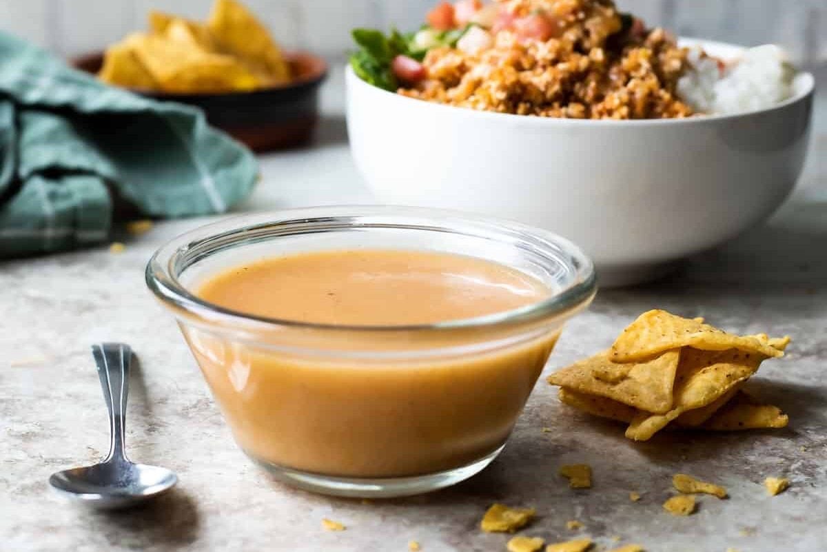 A bowl of Chipotle honey vinaigrette with a Chipotle sofritas burrito bowl in the background.