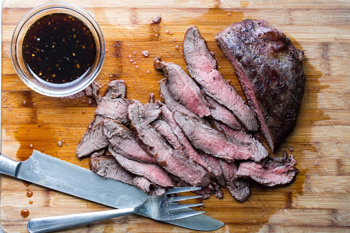 Slicing Hibachi steak on a wooden cutting board.