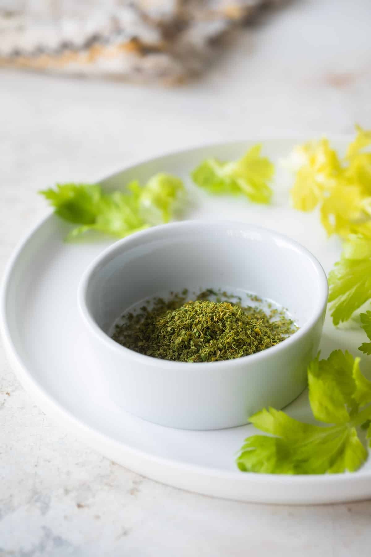 Celery salt in a small white bowl that is resting on a white plate.