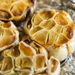 Bulbs of roasted garlic on a piece of crumpled aluminum foil.