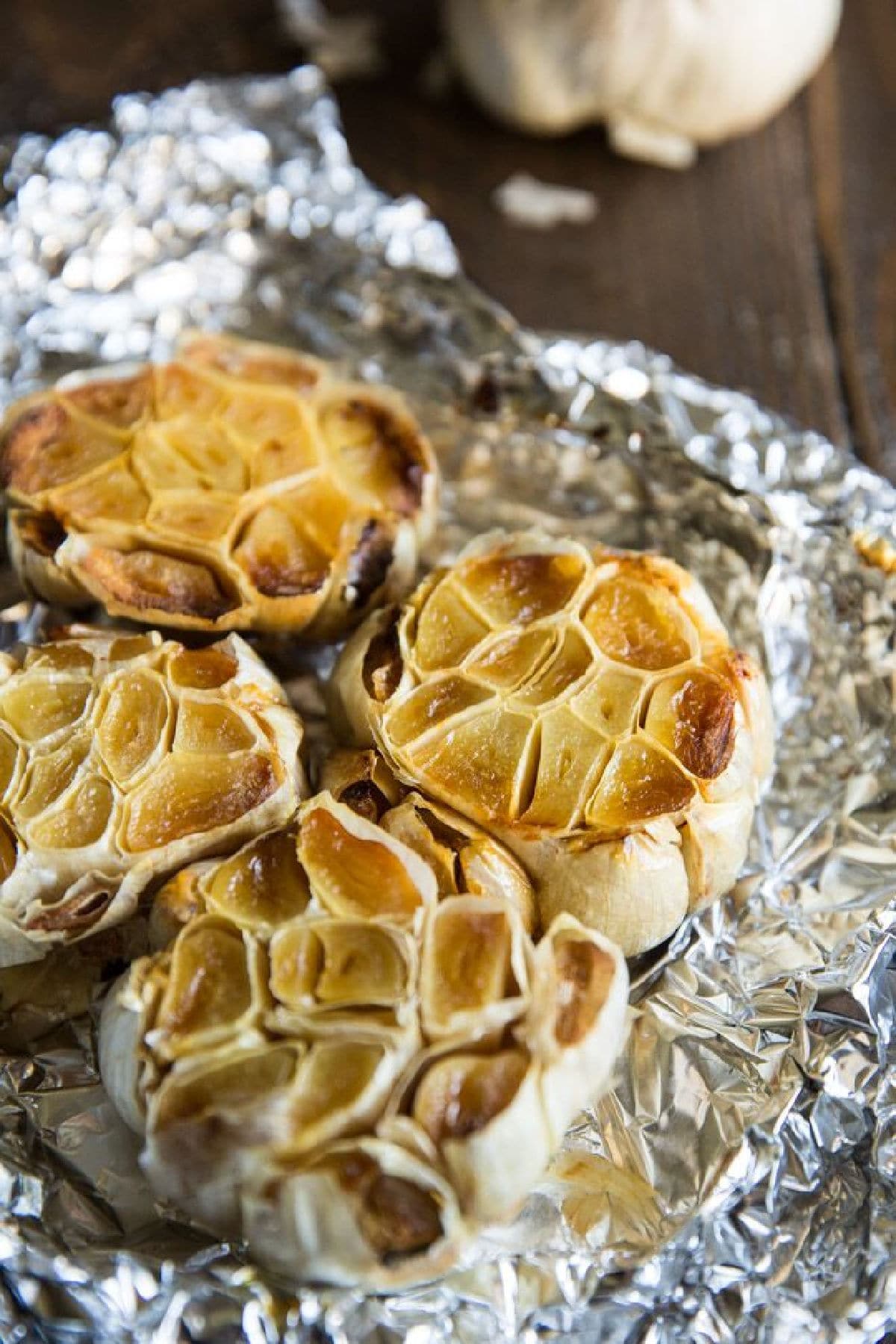 Bulbs of roasted garlic on a piece of crumpled aluminum foil.