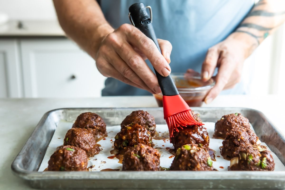 Someone brushing sauce onto Korean meatballs.