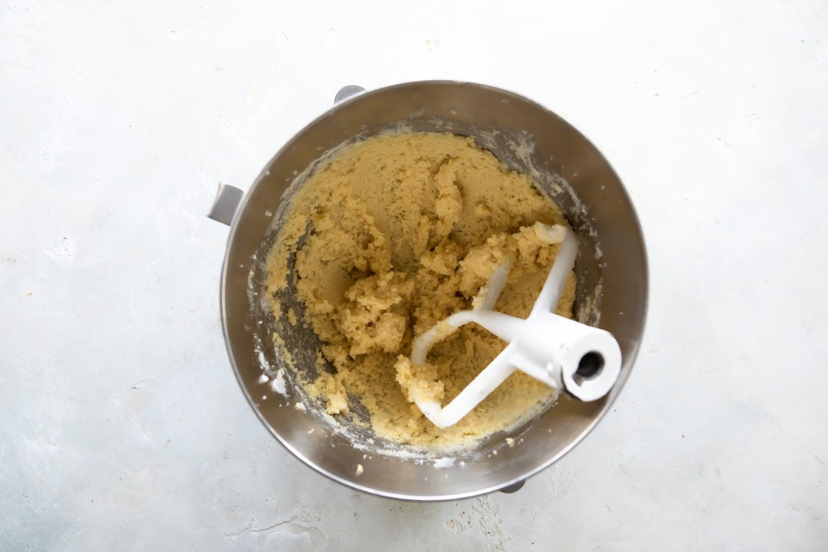 Linzer cookie dough in a silver mixing bowl with a beater attachment resting in it.