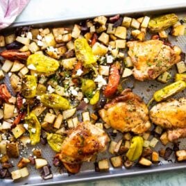 Sheet pan Greek chicken being set on a countertop.