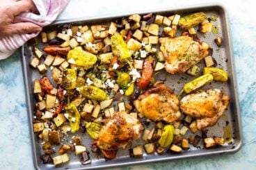 Sheet pan Greek chicken being set on a countertop.