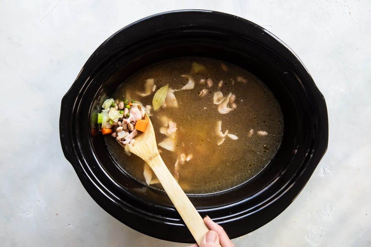 Someone scooping a wooden spoonful of soup out of a slow cooker.