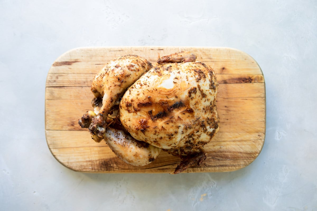 A whole rotisserie chicken on a wooden cutting board.