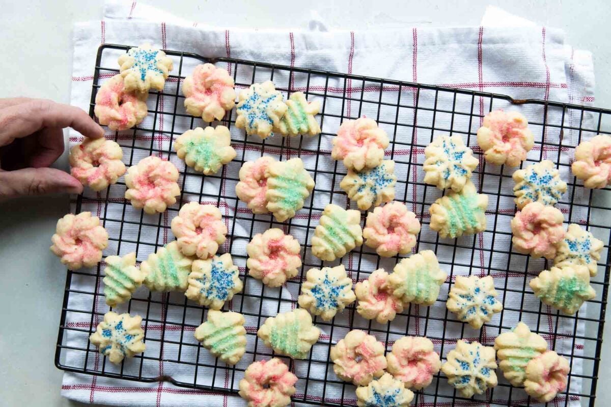 Someone taking a spritz cookie off of a metal cooling rack.