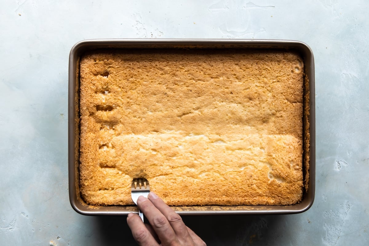 Someone poking holes with a fork into an angel food cake.
