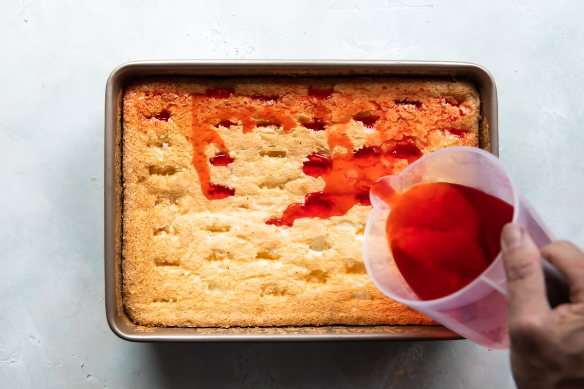 Someone pouring jello liquid into the angel food cake.