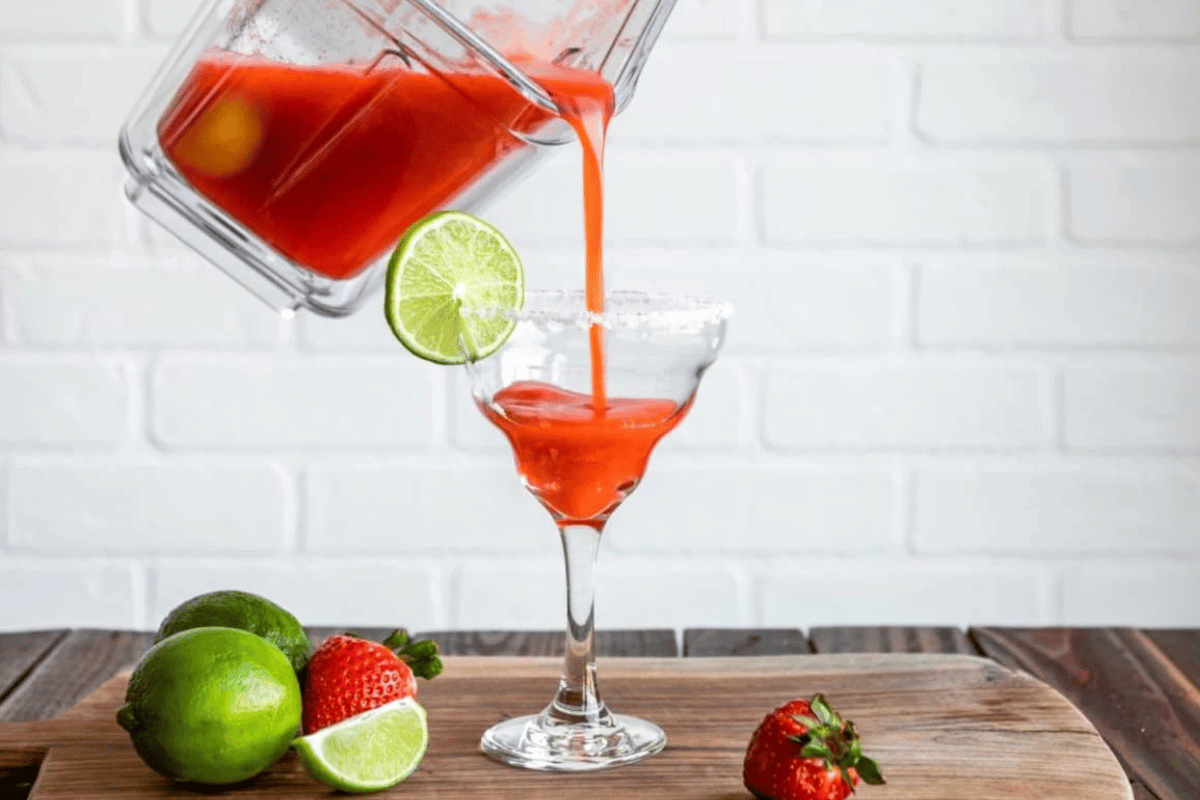 Someone pouring a strawberry margarita into a margarita glass.