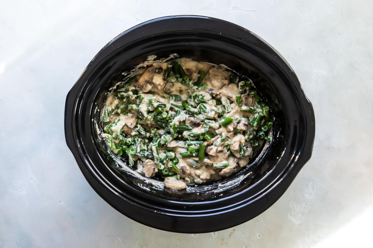Vegan green bean casserole in a black slow cooker before being cooked.