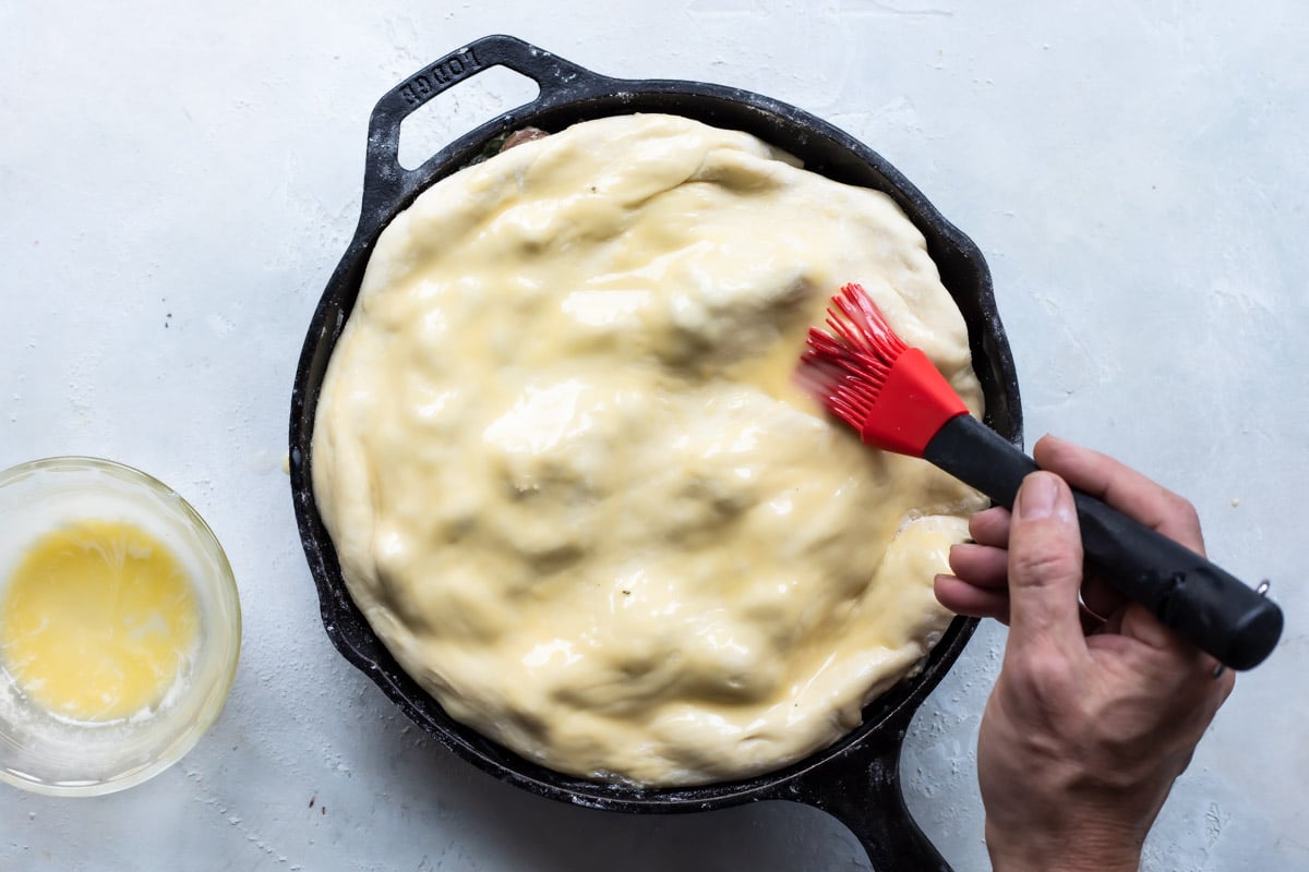Someone brushing vegan egg wash on the top of the vegetable pot pie.