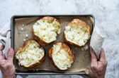 Someone holding a pan with four air fryer baked potatoes.