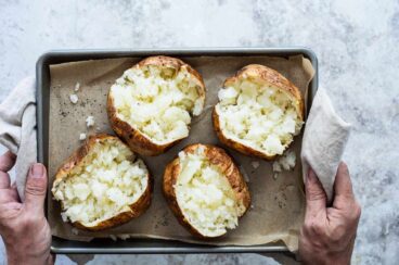Someone holding a pan with four air fryer baked potatoes.