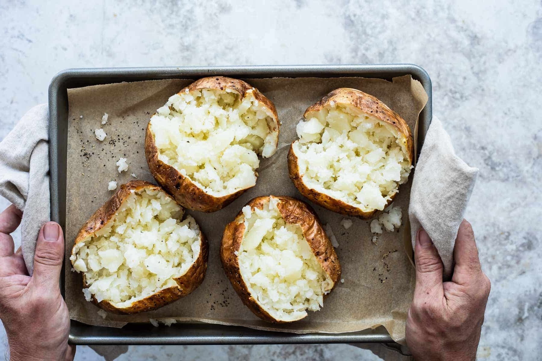 Someone holding a pan with four air fryer baked potatoes.