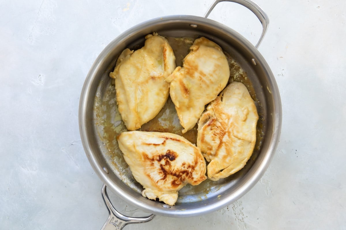Four chicken breasts in a metal skilllet.