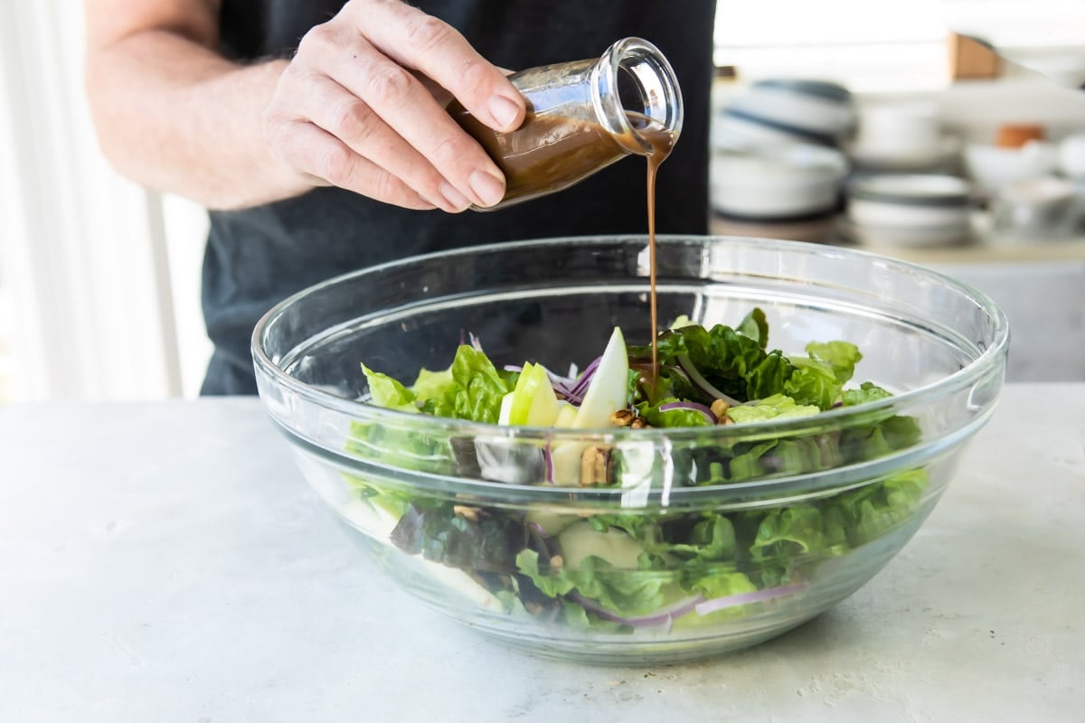Someone drizzling dressing over a bowl of apple walnut salad.