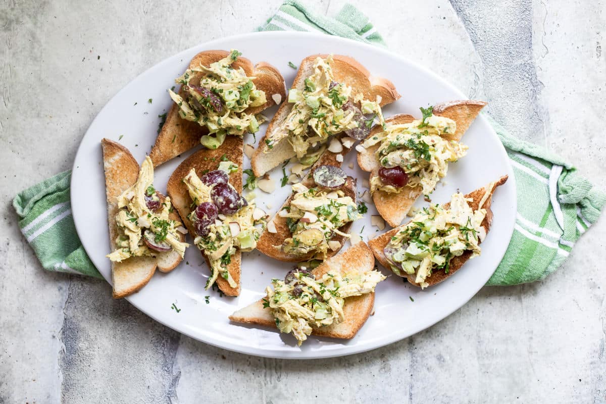 A white plate on top of a green napkin with toasts that have curried chicken salad on top of them.