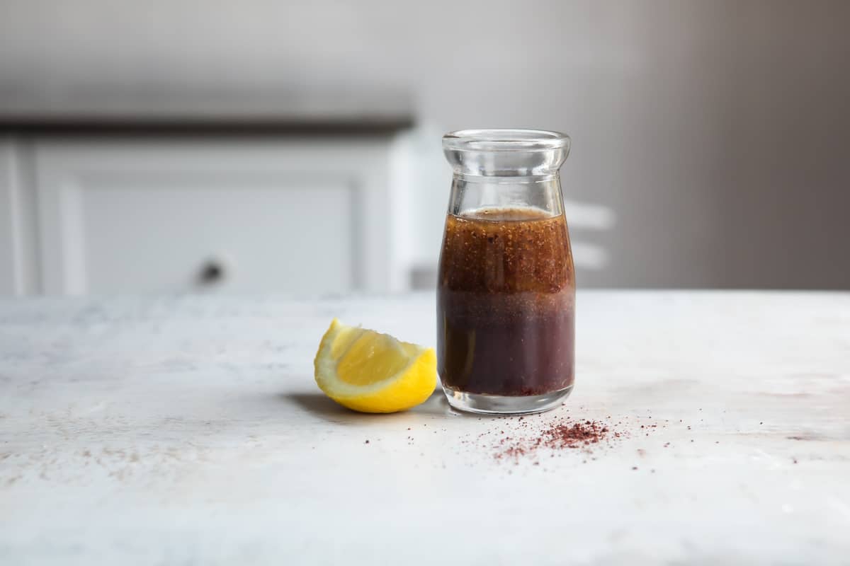 A small clear bottle of salad dressing for Fattoush next to a piece of lemon.
