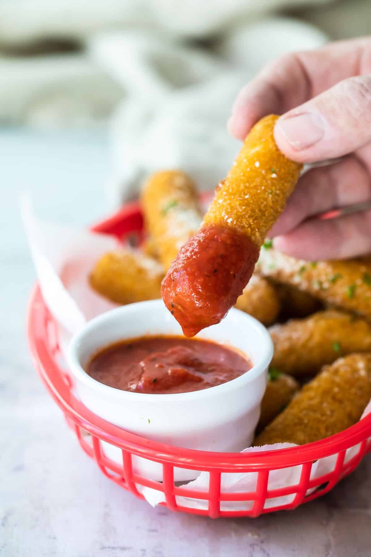 Somebody dipping a mozzarella stick into marinara sauce.