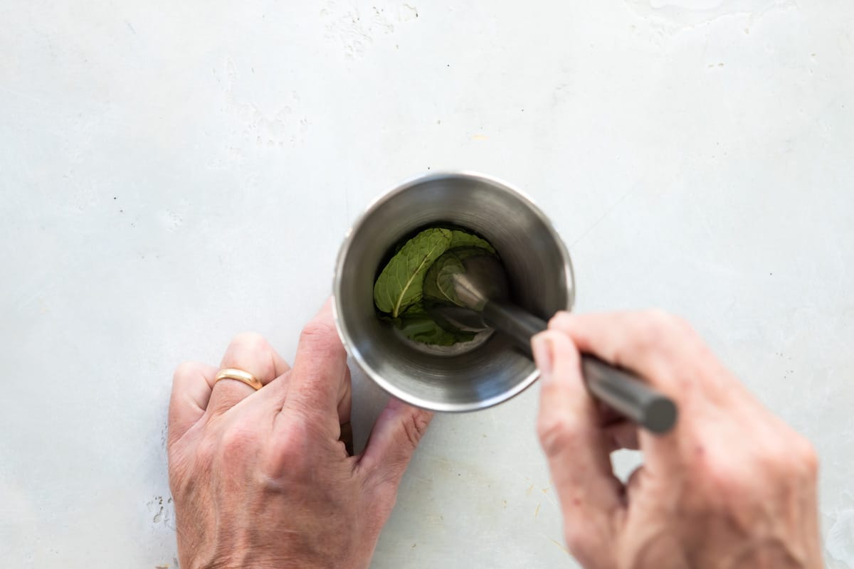 Someone muddling mint in a silver cup.
