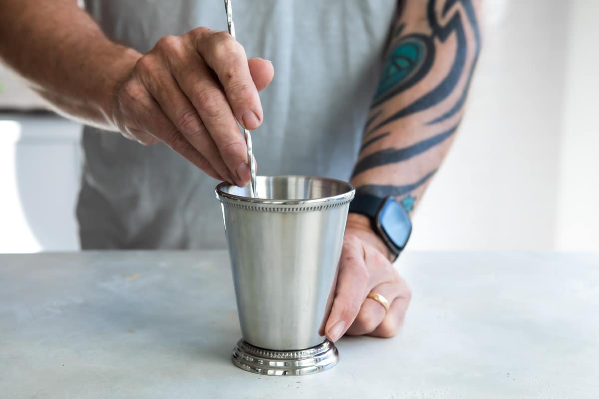 Someone mixing a mint julep in a silver cup.