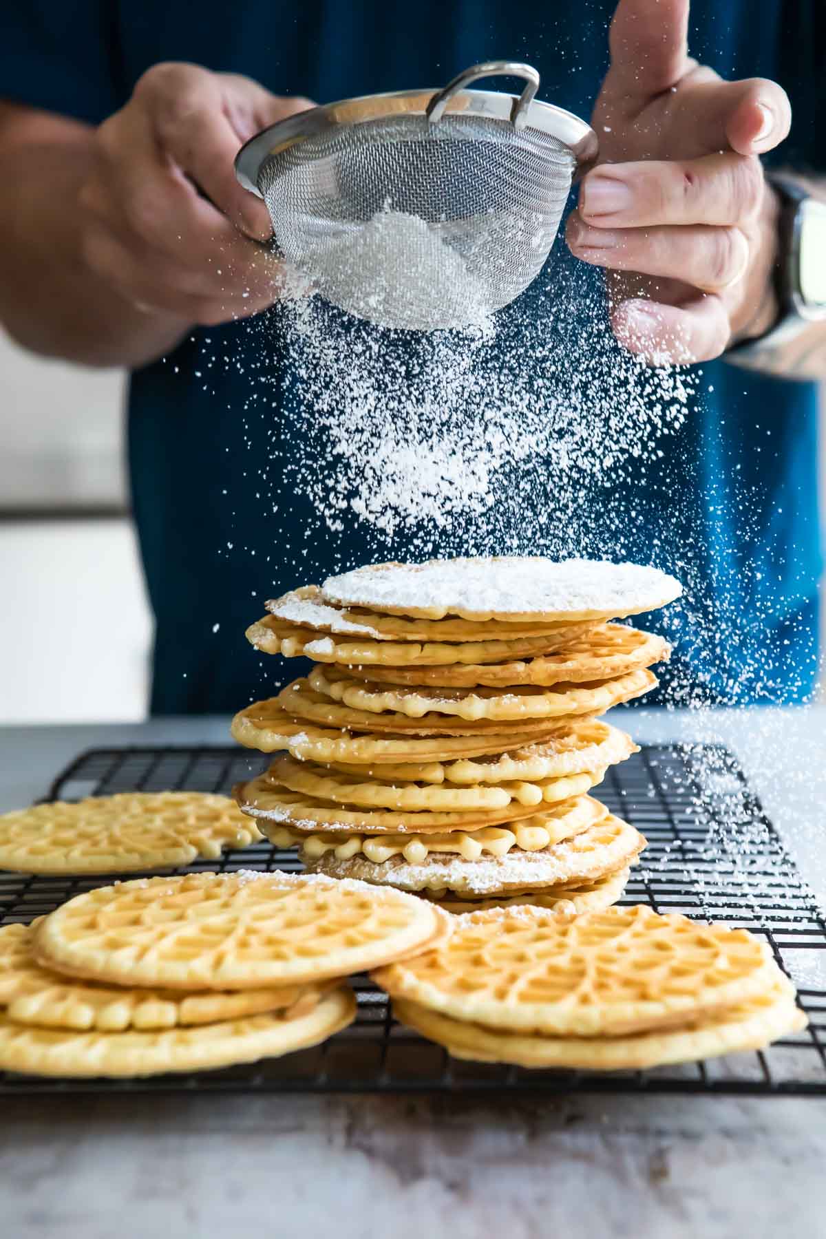Dusting Pizzelle cookies with powdered sugar.