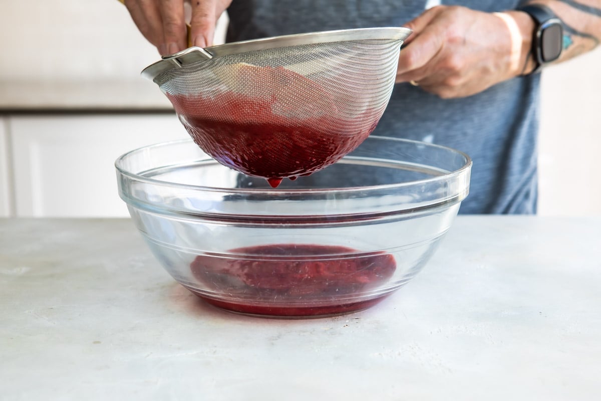 Straining cooked raspberries to remove seeds.