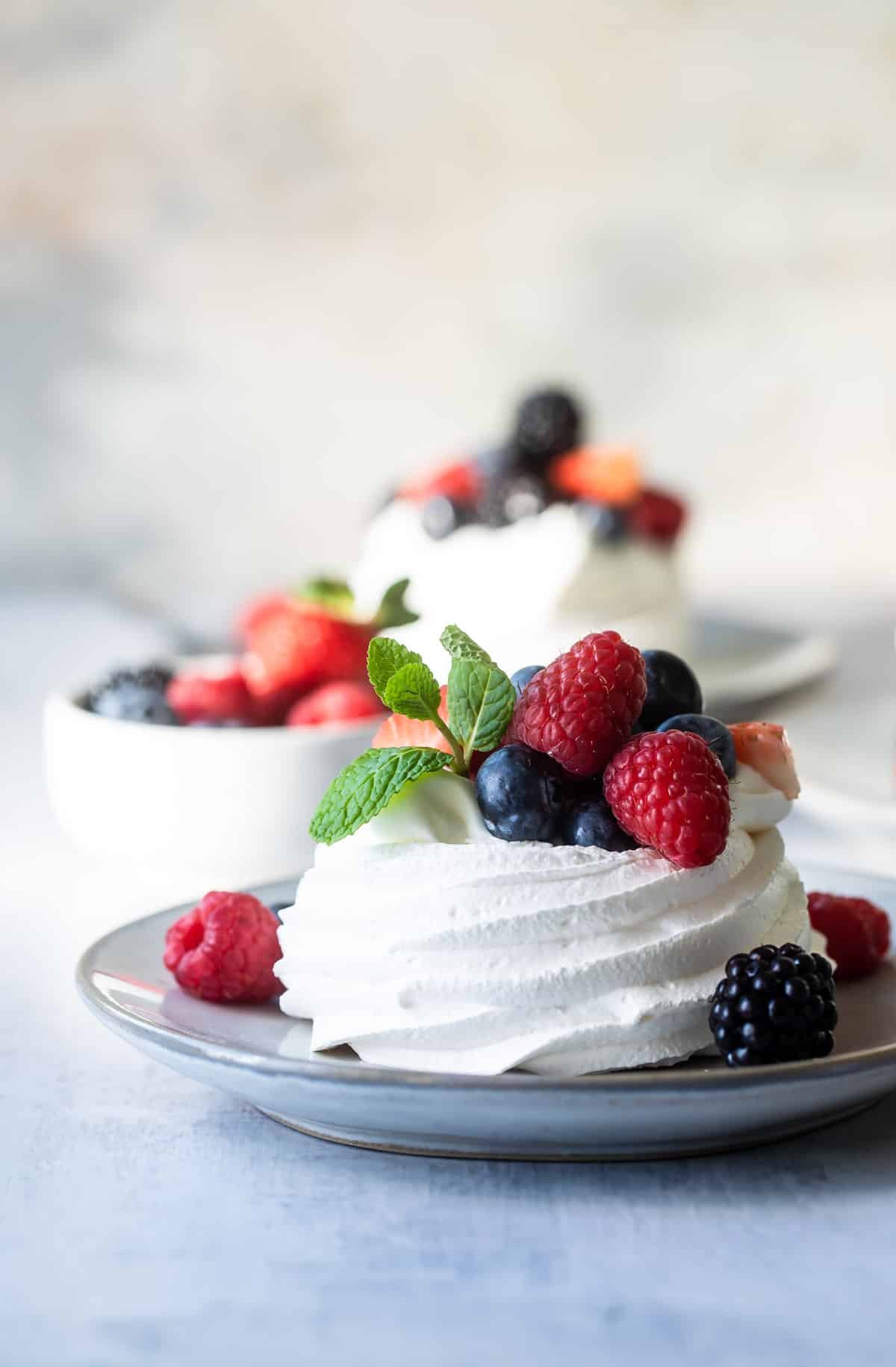 A Schaum torte covered in berries on a gray plate.