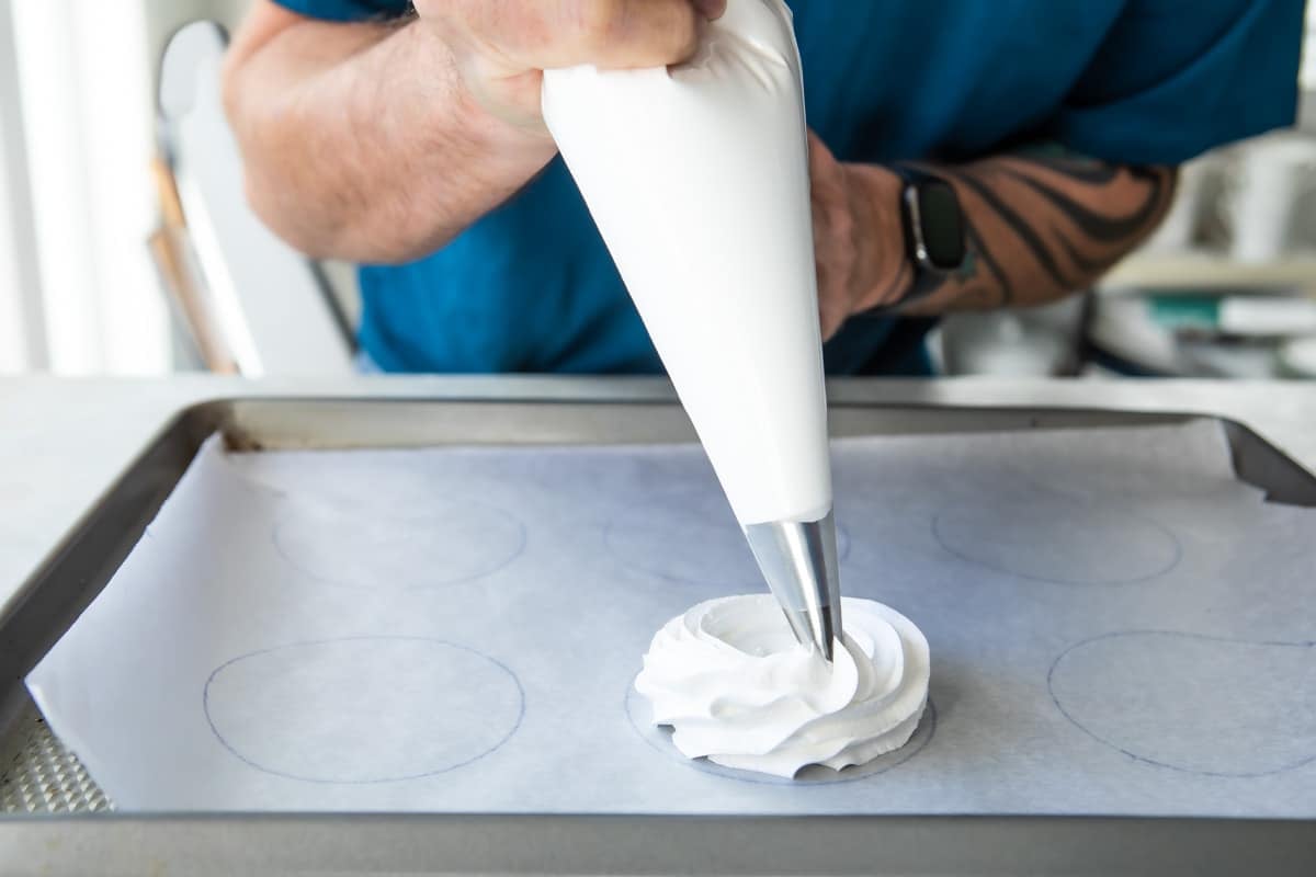 Schaum tortes being piped onto a parchment paper lined baking sheet.