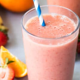 2 glasses with straws of Strawberry Citrus Ginger Smoothie next to fresh fruit.