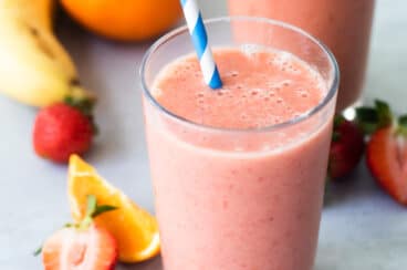 2 glasses with straws of Strawberry Citrus Ginger Smoothie next to fresh fruit.