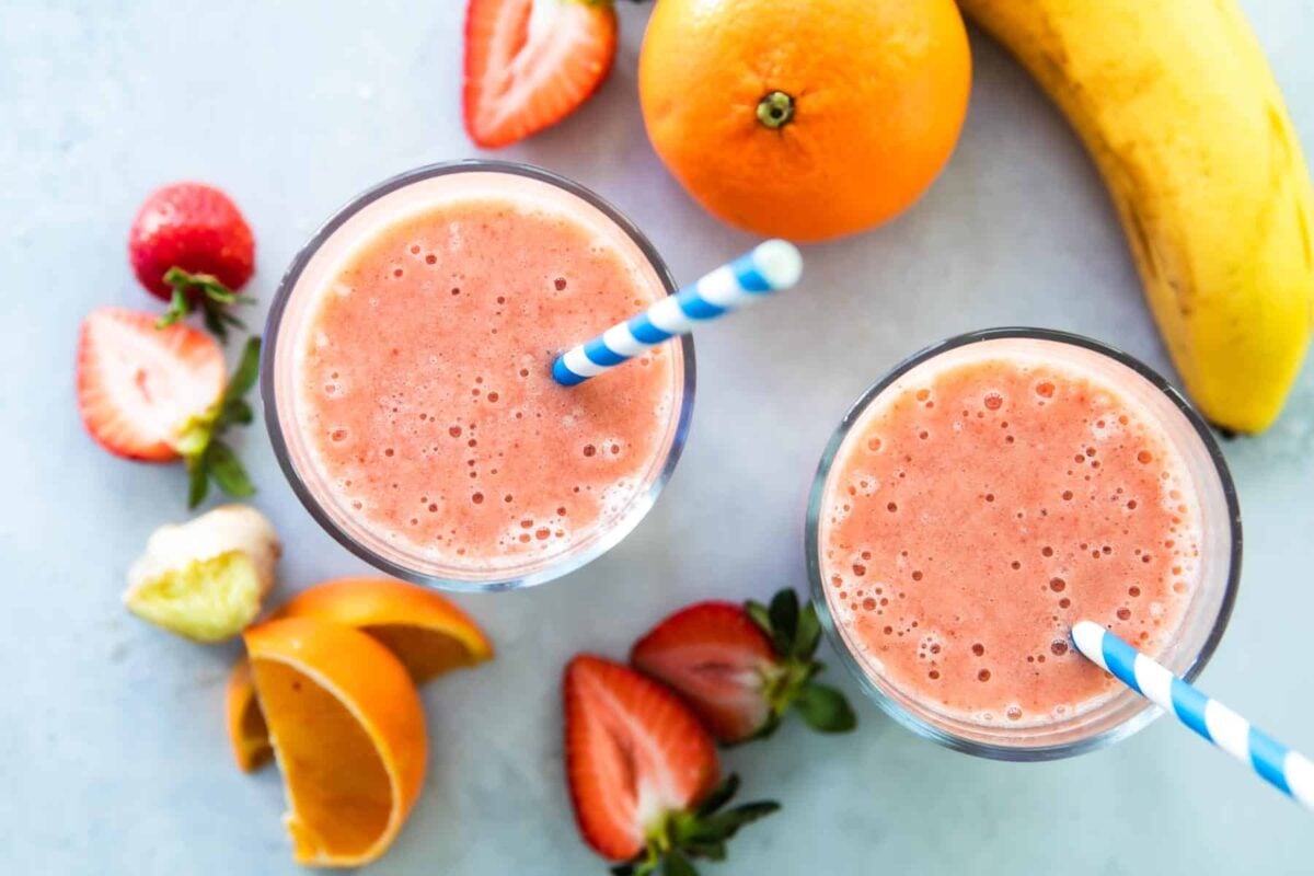 2 glasses with straws of Strawberry Citrus Ginger Smoothie next to fresh fruit.