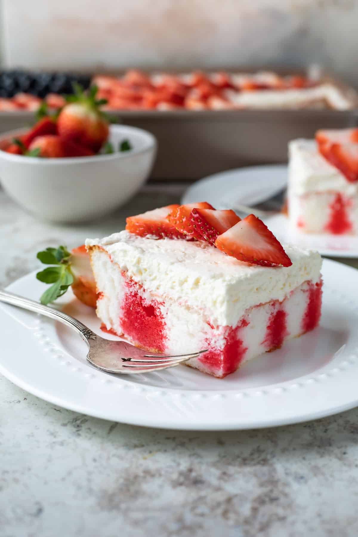 A slice of strawberry jello poke cake on a white plate.
