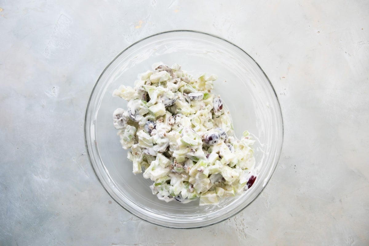 Waldorf salad being after being mixed in a clear glass bowl.