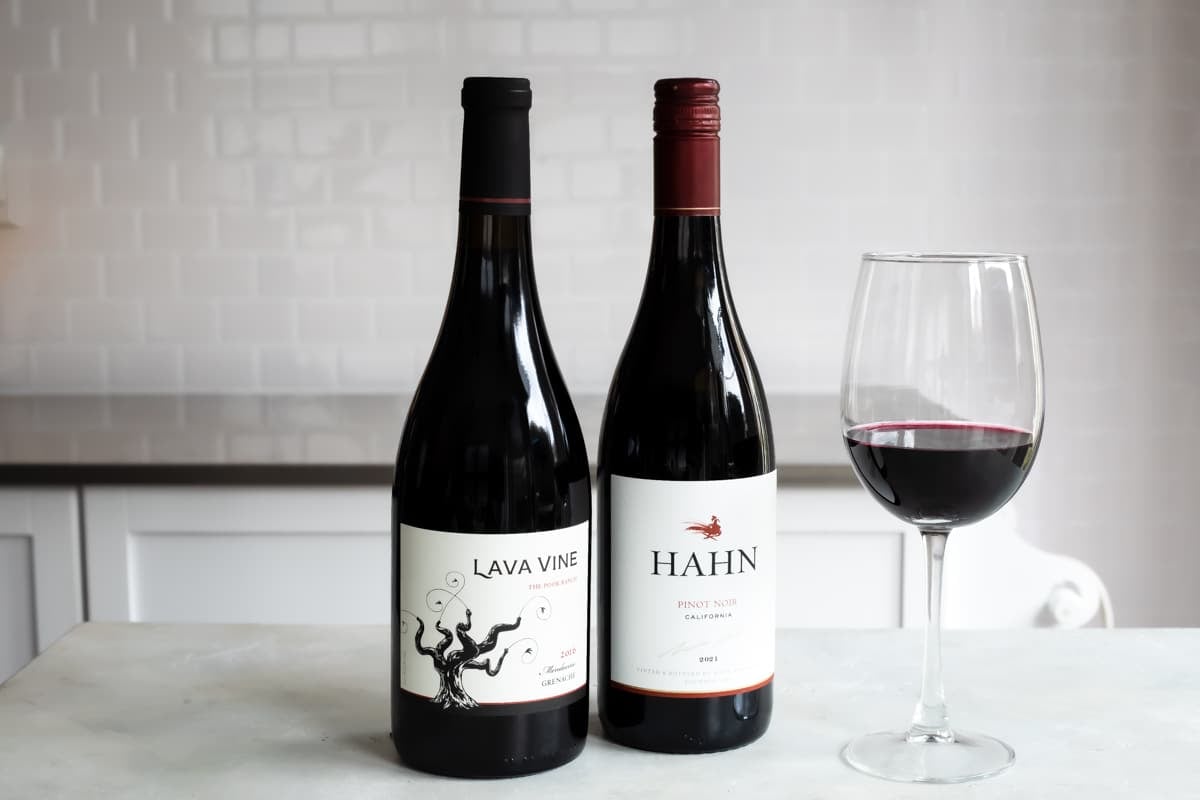 Two bottles of red wine next to a glass of the same.