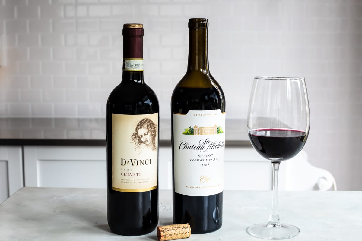 Two bottles of red wine next to a glass of the same.