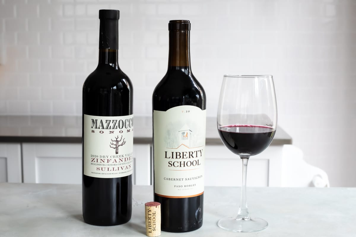 Two bottles of red wine next to a glass of the same.