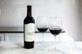 A bottle of red wine next to 2 glasses of the same.